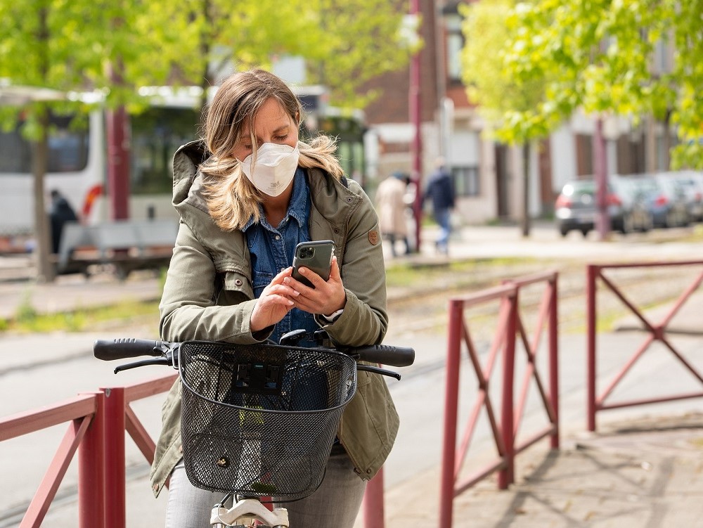 Eine Frau mit Schutzmaske auf einem Fahrrad gelehnt schaut auf ihr Smartphone