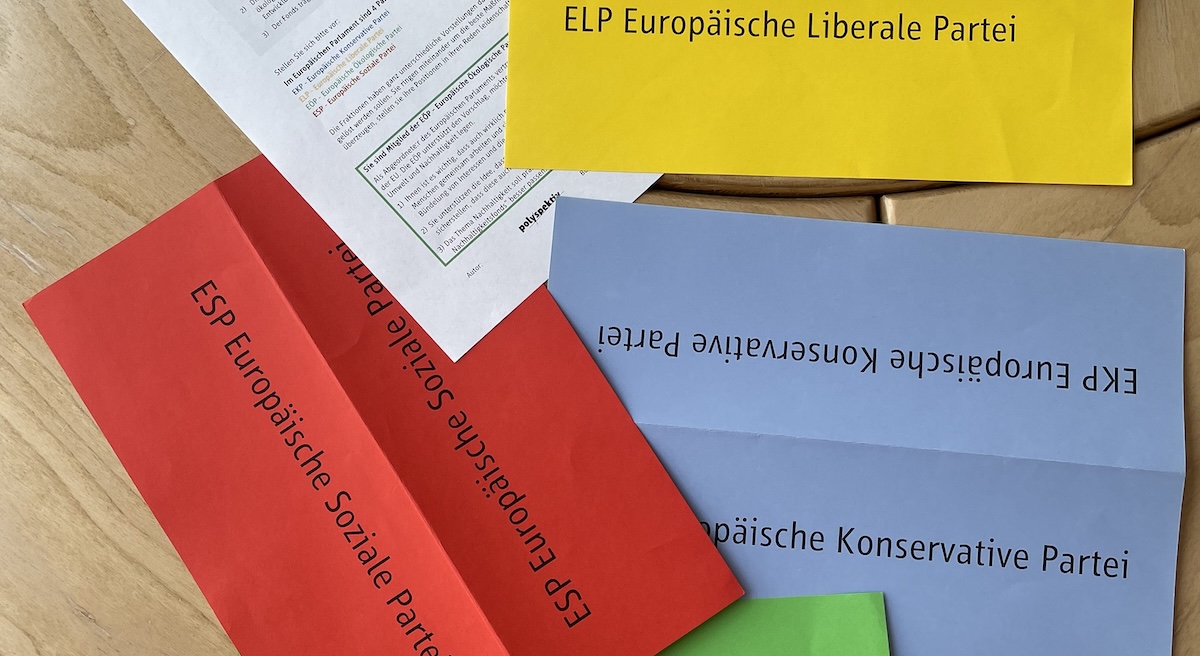 Foto mit Teilen von Materialien des Planspiels: Blatt mit der Beschreibung der Aufgabe sowie einem gelben, blauen, grünen und roten Schild mit fiktiven Parteinamen