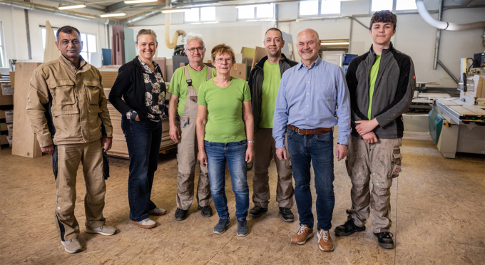 Gruppe von acht Mitarbeitenden der Möbel-Damm GmbH in einer Werkstatt mit Maschinen im Hintergrund