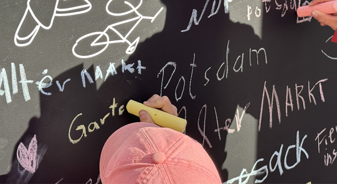 Zwei Hände beschreiben mit Kreide die Rückseite des Projektsrades am EFRE/JTF-Stand