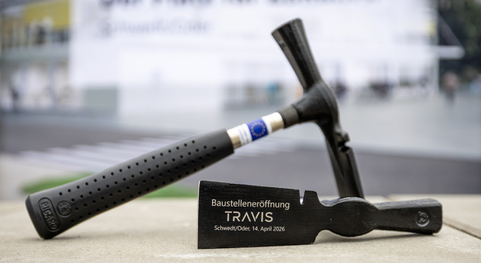 Zwei schwarze Hämmer liegen auf einer grauen Oberfläche, einer steht aufrecht, der andere liegt flach mit der Aufschrift "Baustelleneröffnung TRAVIS Schwedt/Oder, 14. April 2026"